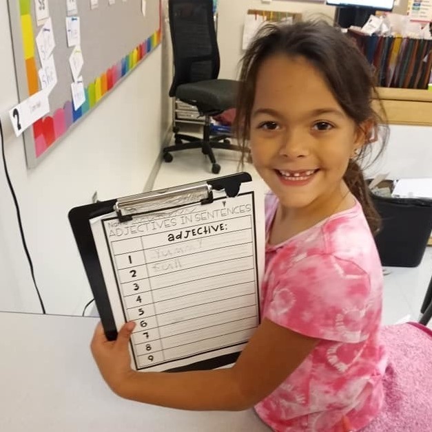 Student smiling with a list of adjectives on a clipboard