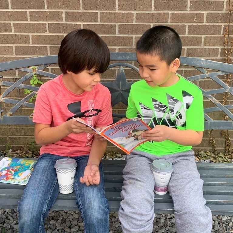 two students buddy reading outside
