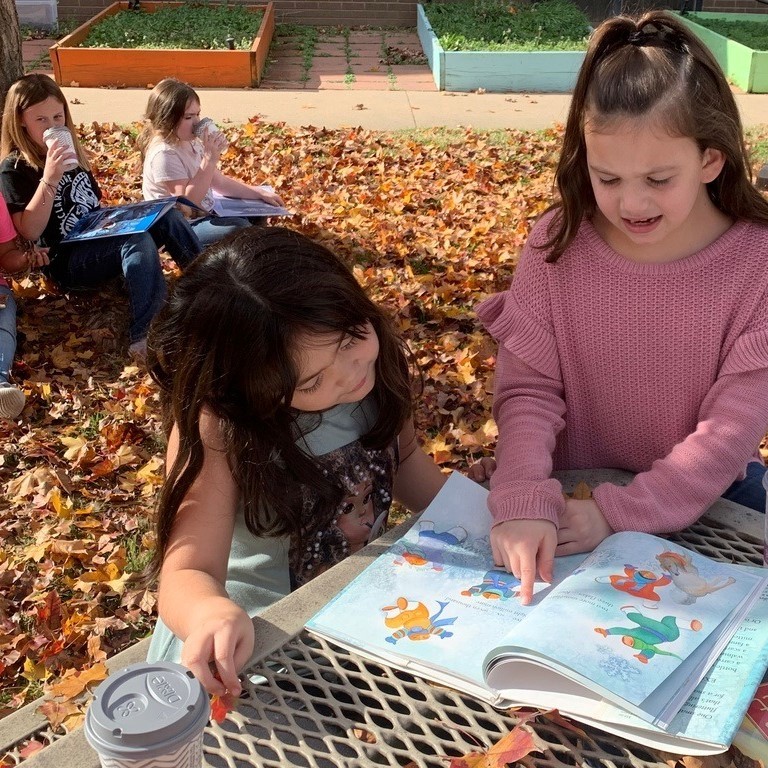 two students buddy reading outside 